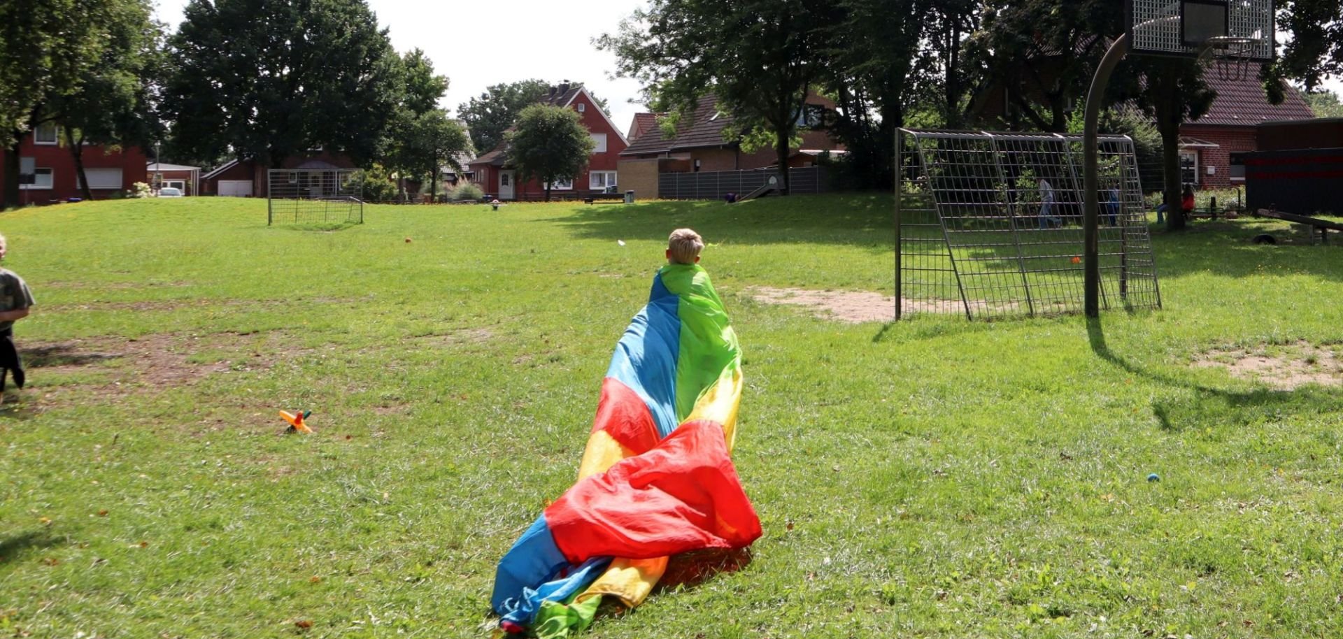 Ein Kind läuft mit einem großen bunten Tuch über einen Spielplatz