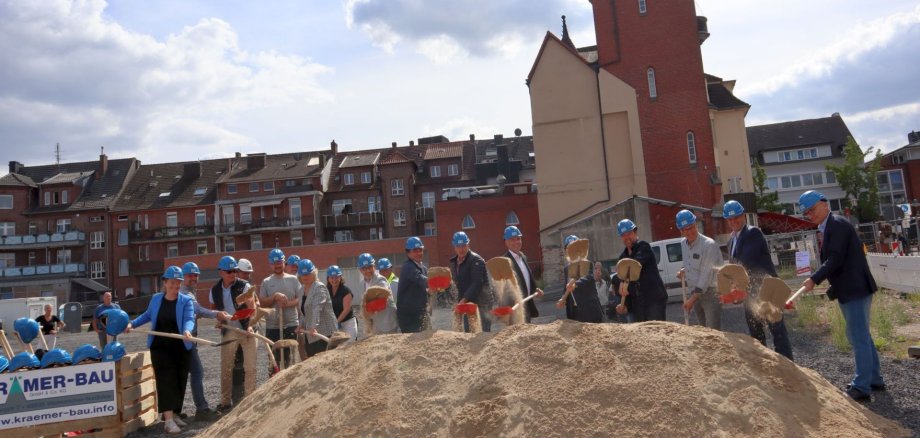 Gruppe von Menschen mit Bauhelmen und Spaten auf der Baustelle an der Bahnhofstraße 