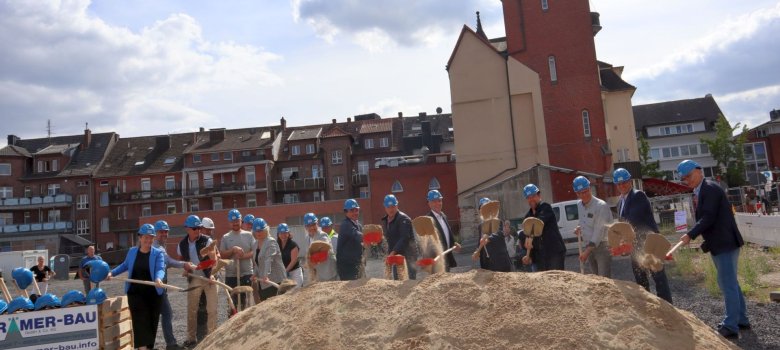 Gruppe von Menschen mit Bauhelmen und Spaten auf der Baustelle an der Bahnhofstraße 