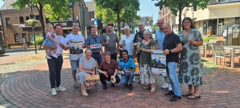 Eine Gruppe von Akteuren am Eper Brunnen mit Plakaten zum Eper Weinfest Akteure freuen sich auf das 3. Eper Weinfest und das Brunnenfest im Eper Ortskern.
