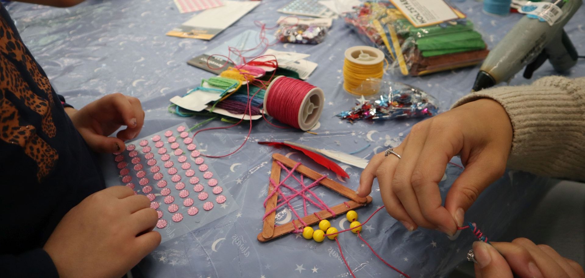 Eine Betreuerin hilft einem Kind beim Basteln von Traumfängern