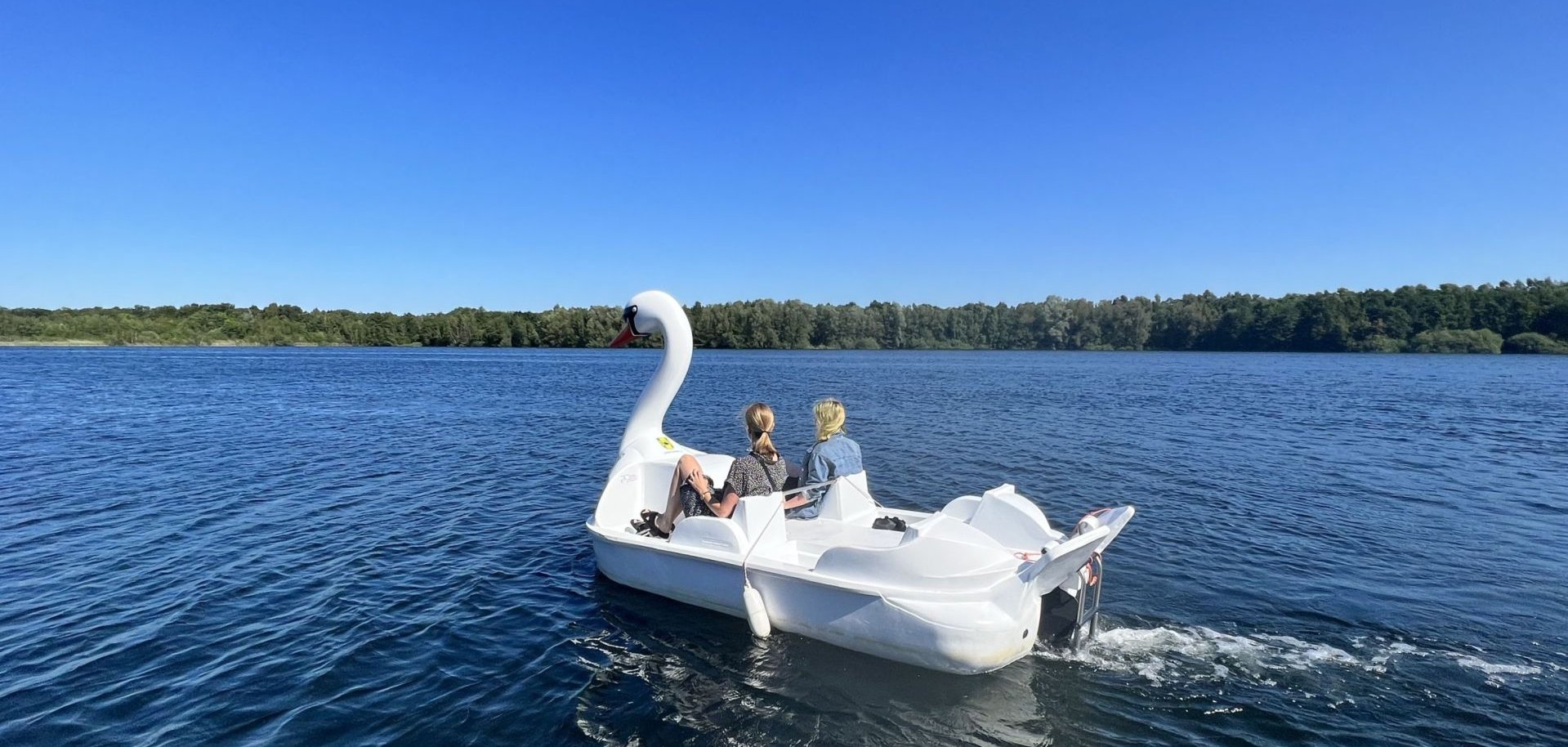 Zwei Personen fahren in einem Schwan-Tretboot über den Dreiländersee.