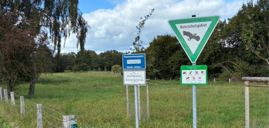 Ein Schild weist auf das Naturschutzgebiet hin, das im Hintergrund zu sehen ist Ein Schild weist auf das Naturschutzgebiet hin, das im Hintergrund zu sehen ist
