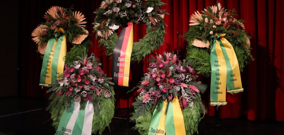Kränze mit Trockenblumen und Gedenkbändern vor einem roten Vorhang. Kränze mit Trockenblumen und Gedenkbändern vor einem roten Vorhang.