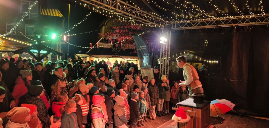 Auf der Bühne des Eper Weihnachtsmarkts tritt eine Person auf und begeistert viele gespannt zuschauende Kinder und Erwachsene
