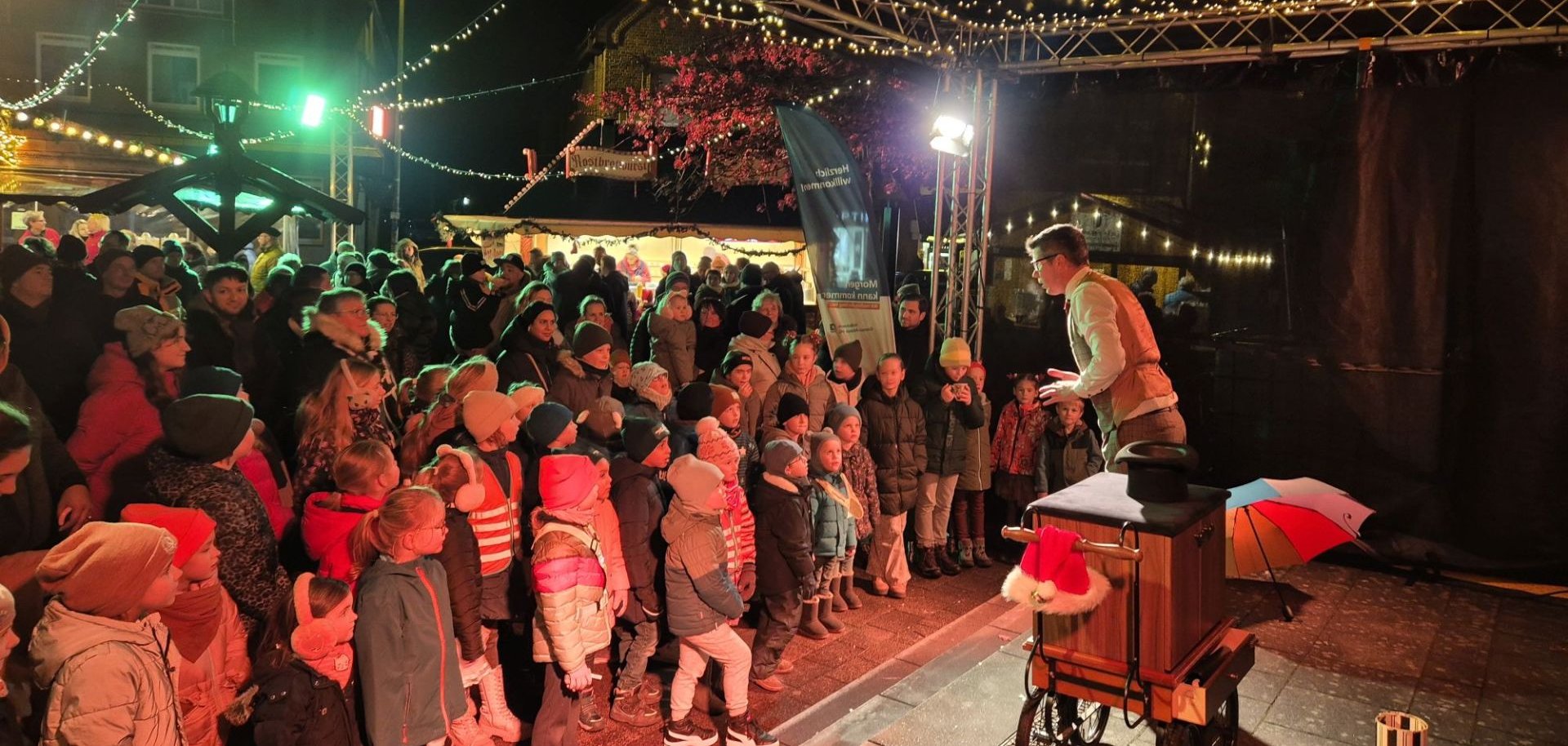 Auf der Bühne des Eper Weihnachtsmarkts tritt eine Person auf und begeistert viele gespannt zuschauende Kinder und Erwachsene