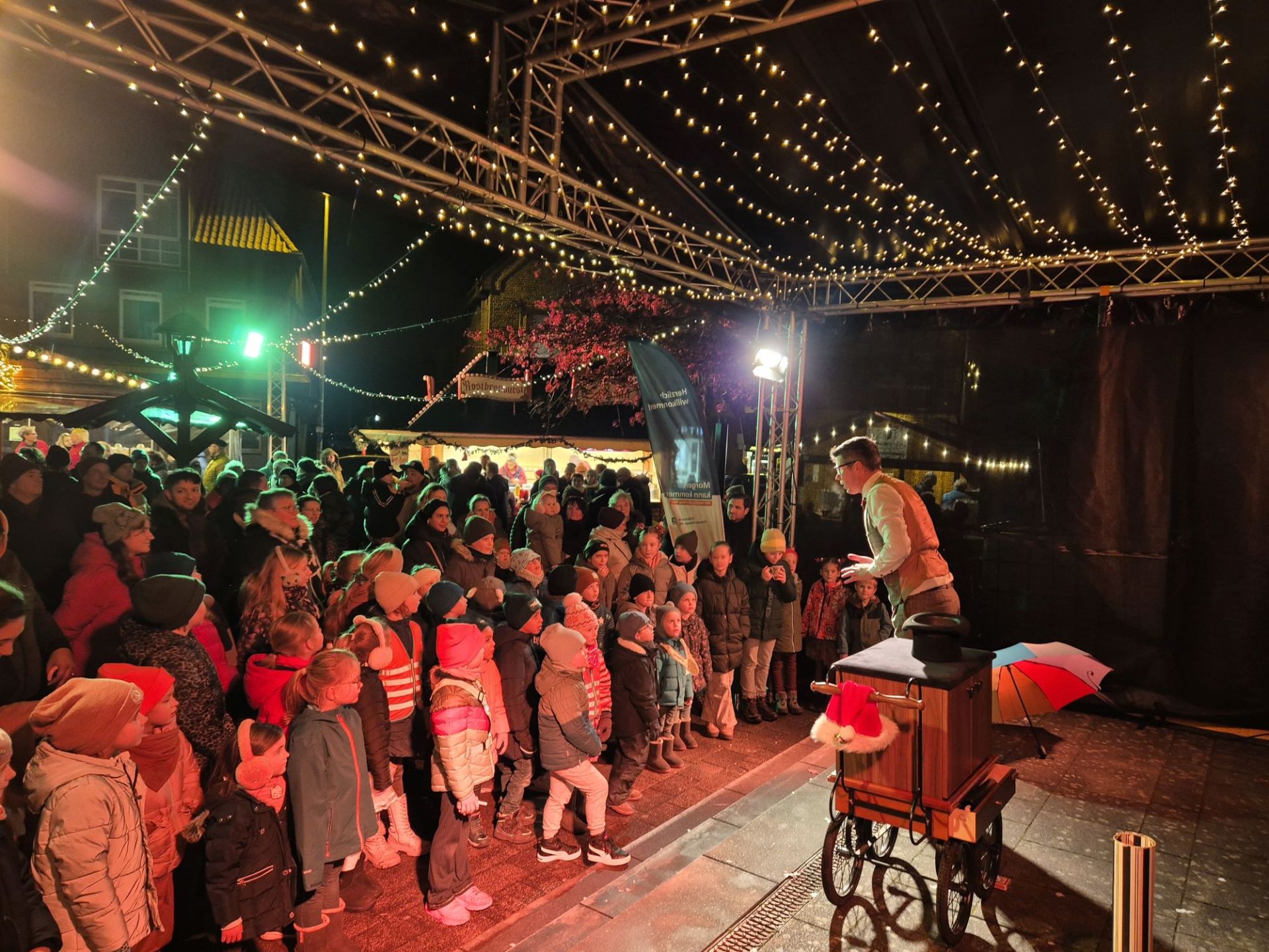 Auf der Bühne des Eper Weihnachtsmarkts tritt eine Person auf und begeistert viele gespannt zuschauende Kinder und Erwachsene