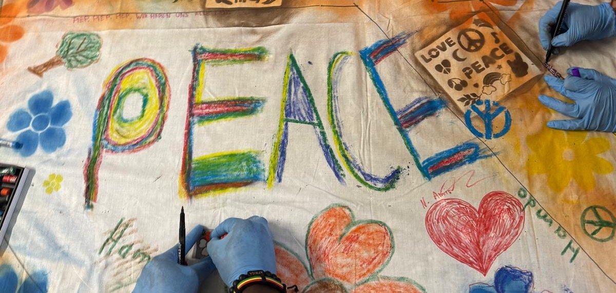 Buntes Banner mit dem Wort „PEACE“, Blumen und Friedenssymbolen