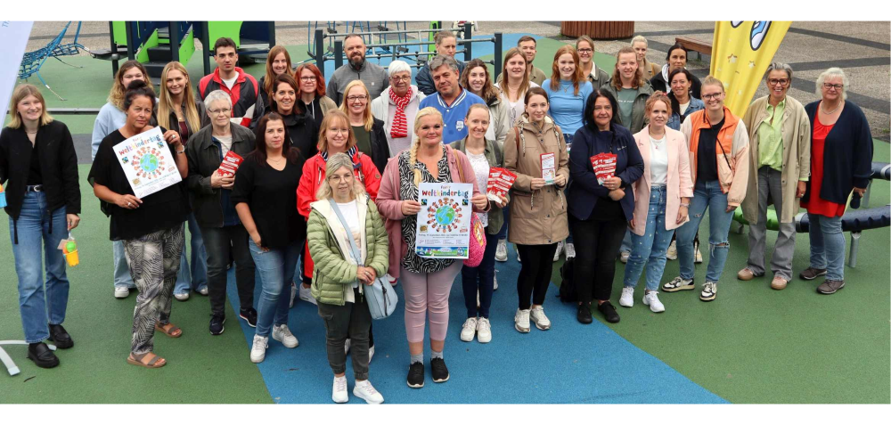 Gruppenfoto auf dem Spielplatz am Kurt-Schumacher-Platz. Einige halten Plakate zum Weltkindertag in den Händen.