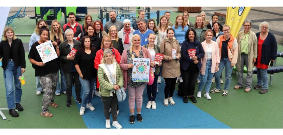 Gruppenfoto auf dem Spielplatz am Kurt-Schumacher-Platz. Einige halten Plakate zum Weltkindertag in den Händen.