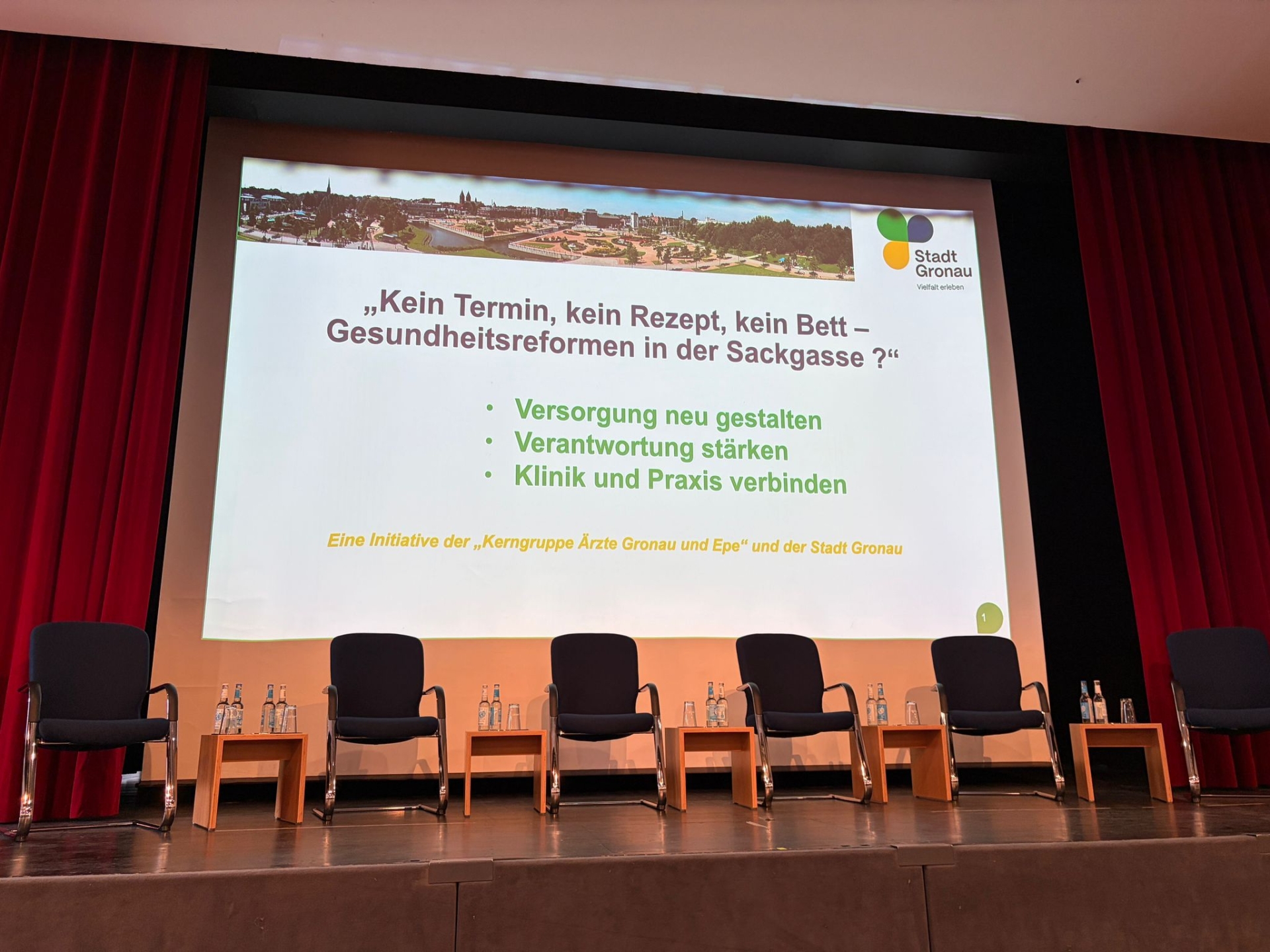 Bühne mit Stuhlreihe und Präsentationsfolie zum Thema Gesundheitsreformen in Gronau