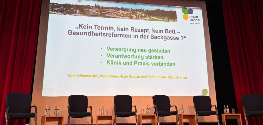 Bühne mit Stuhlreihe und Präsentationsfolie zum Thema Gesundheitsreformen in Gronau