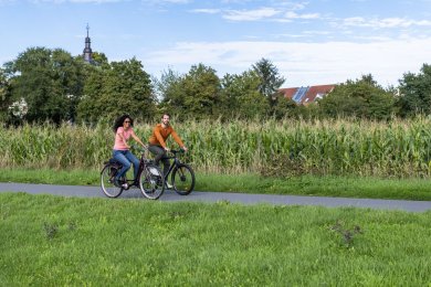 Zwei Personen fahren Fahrrad an einem Feld entlang