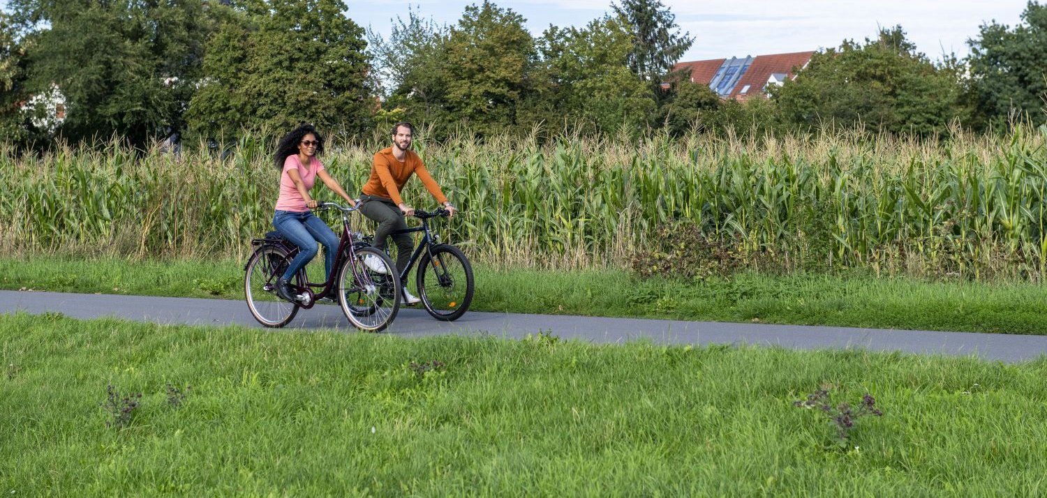 Zwei Personen fahren Fahrrad an einem Feld entlang