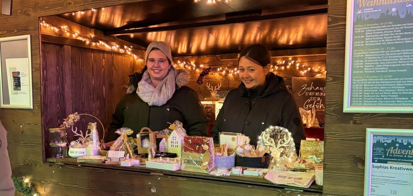 Zwei Personen stehen hinter einem Stand auf dem Weihnachtsmarkt in Epe und bieten gebastelte Sachen an.