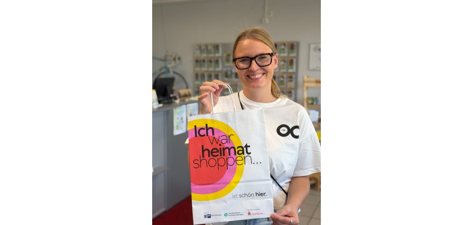 Lena Kerkeling aus dem Stadtmarketing präsentiert die Heimatshoppen-Tüte. Lena Kerkeling aus dem Stadtmarketing zeigt eine Papiertüte mit der Aufschrift "Ich war heimat shoppen... ist schön hier."